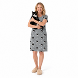 Woman wearing a gray nightgown with black cat pattern, holding a black and white cat on a white background