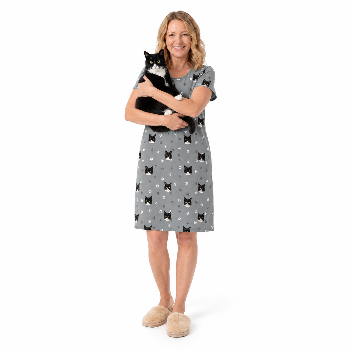 Woman wearing a gray nightgown with black cat pattern, holding a black and white cat on a white background
