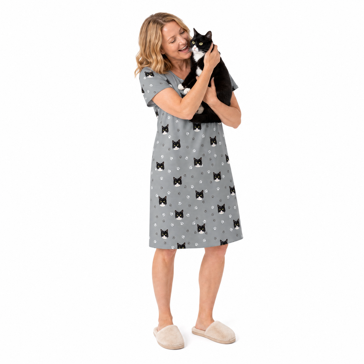 Woman wearing a gray nightgown with black cat patterns, holding a black and white cat on a white background