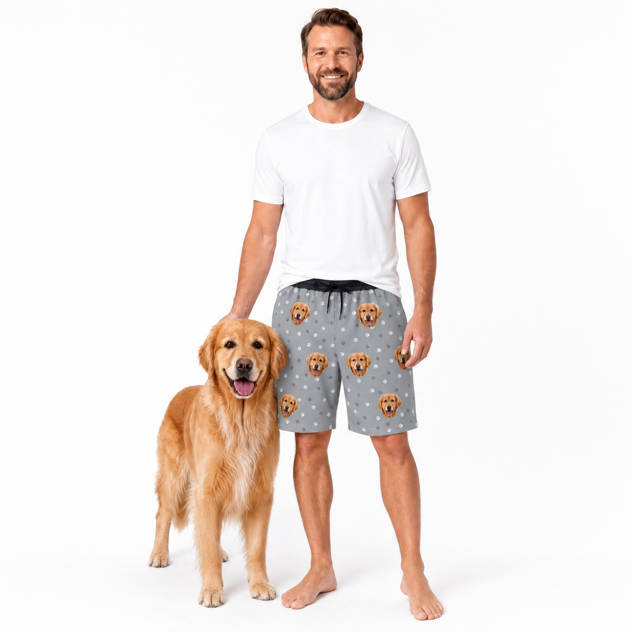 Man wearing gray shorts with dog pattern standing next to a golden retriever on a white background