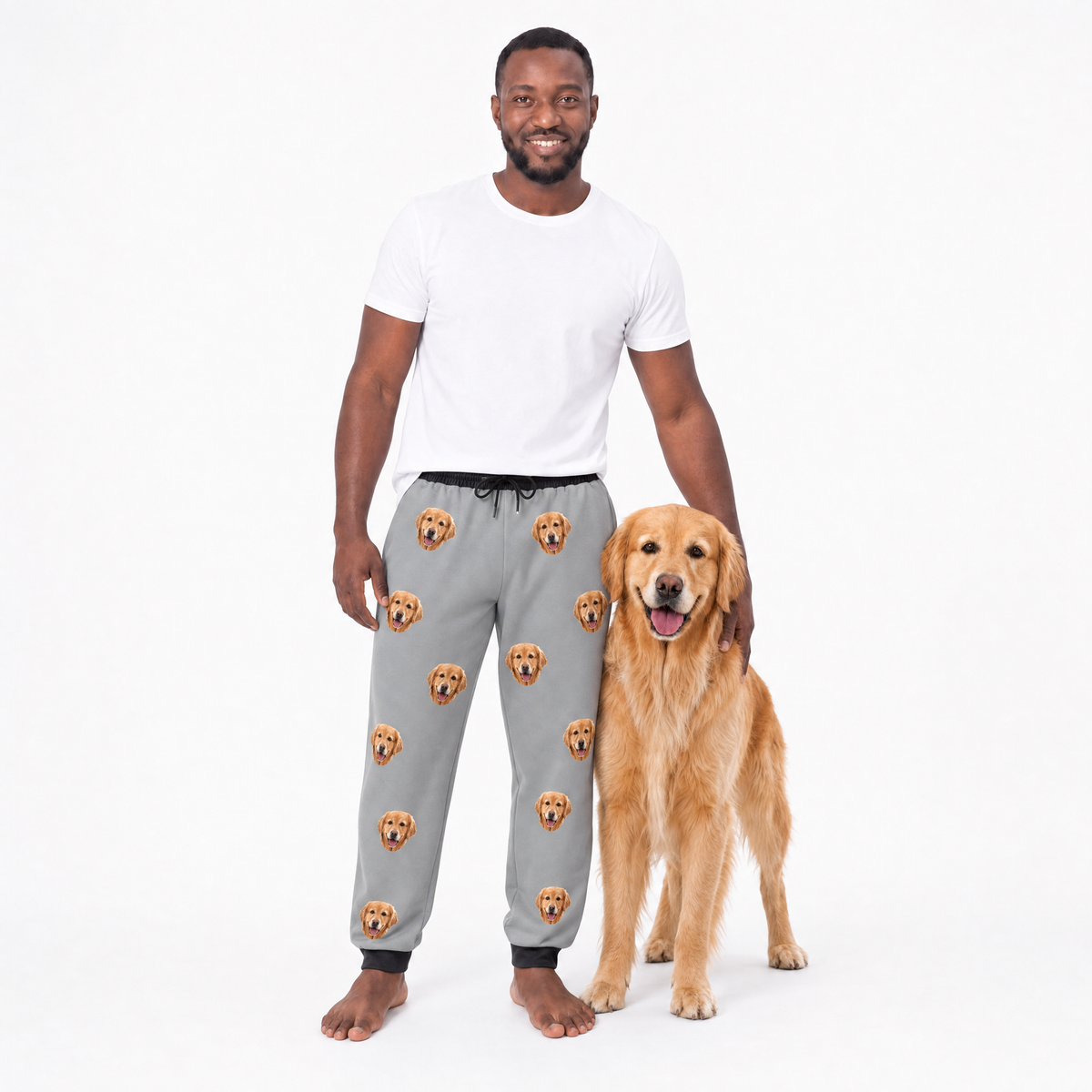 Man wearing gray sweatpants with dog pattern standing next to a golden retriever on a white background