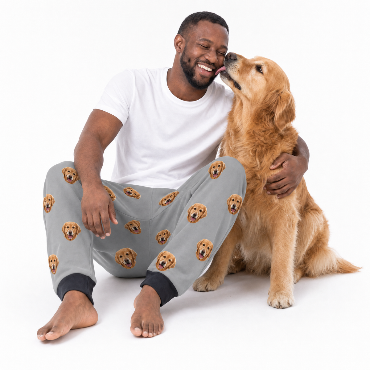 Man wearing sweatpants with dog pattern sitting with a dog on a white background