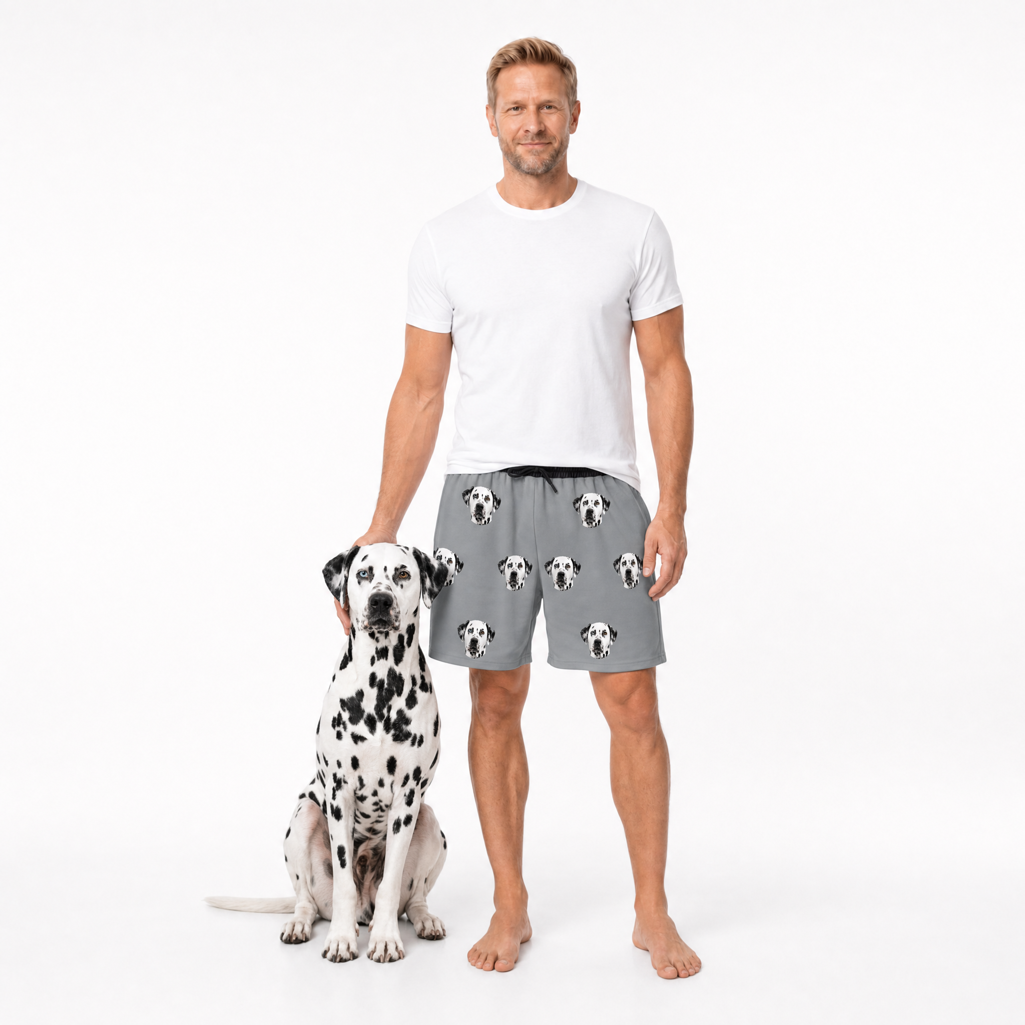 Man wearing a white t-shirt and gray shorts with dog pattern standing next to a Dalmatian dog on a white background