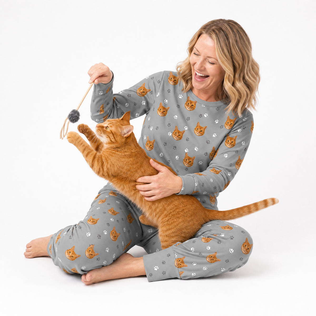Woman in matching jogger pajama set with a cat playing with a toy on a white background