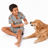 Child wearing a Slate Gray dog-print pajama short set sitting on the floor and playing tug with a golden retriever.