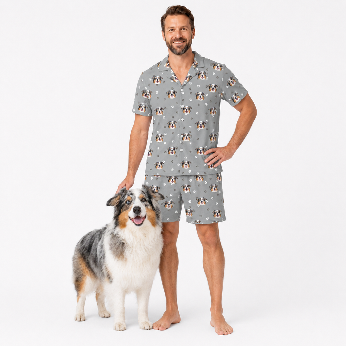Man wearing a gray pajama set with dog pattern standing next to a dog on a white background