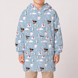 A child wearing a light blue hooded sweatshirt with an all-over Christmas dog and snowman print, paired with beige pants, against a plain light gray background.