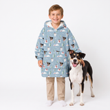 A young boy wearing a light blue hooded fleece jacket with a dog print pattern, standing next to a black and white dog on a white studio background.