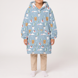 A child wearing a light blue hooded sweatshirt with an all-over winter dog print, paired with beige pants and white socks, standing against a plain light gray studio background.