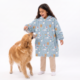 A young girl wearing a light blue fleece pajama robe with a dog print pattern stands next to a golden retriever dog on a white studio background.