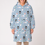 A woman wearing a light blue hooded sweatshirt dress with a winter print of black and white cats, snowmen, pine trees, and snowflakes, shown against a plain light gray background.