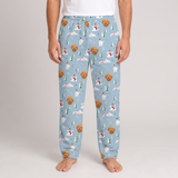 A person wearing light blue pajama pants with a repeating print of golden retriever dogs, snowmen, evergreen trees, and snowy mountains, shown against a plain light gray studio background.