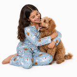 A young girl with long dark hair sits on a white studio floor hugging a fluffy brown dog. She is wearing light blue pajamas with a holiday print featuring snowmen, Christmas trees, and gingerbread cookies.