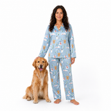 A woman wearing a light blue long-sleeve pajama set with a dog print stands next to a golden retriever dog on a plain white background.