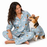 A woman and a corgi dog wearing matching light blue pajamas with a festive holiday print of Santa Claus, snowman, Christmas trees, and dogs, posed together on a white studio background.