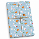 A rectangular gift box wrapped in light blue holiday-themed wrapping paper with a repeating pattern of corgis, Santa clowns, and Christmas trees, tied with a brown twine bow in the center.