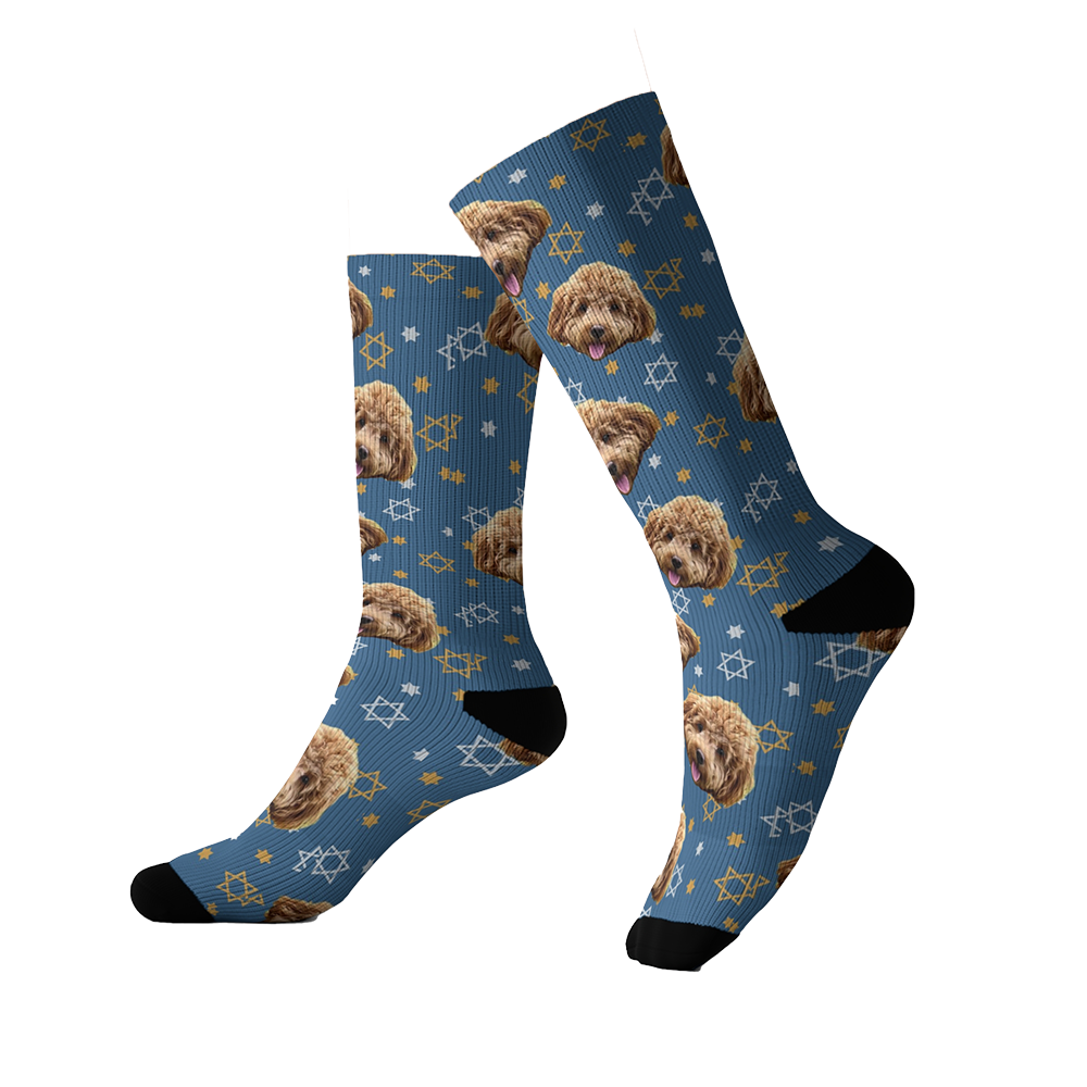 Blue crew socks decorated with repeating images of a curly-haired brown dog’s face and white and gold Stars of David, featuring black heels and toes.