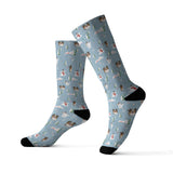 A pair of ribbed crew socks in light blue with a repeating print of small brown and white dogs, pink clouds, and green trees, finished with solid black heels, toes, and cuffs, shown on a white background.