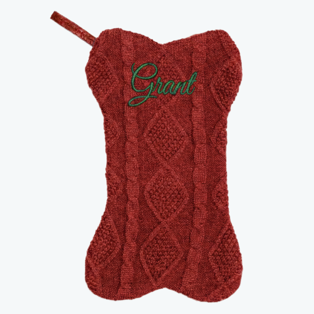 Red knitted dog-bone–shaped Christmas stocking with a cable knit pattern and the name ‘Grant’ embroidered in green script at the top, featuring a matching red hanging loop.