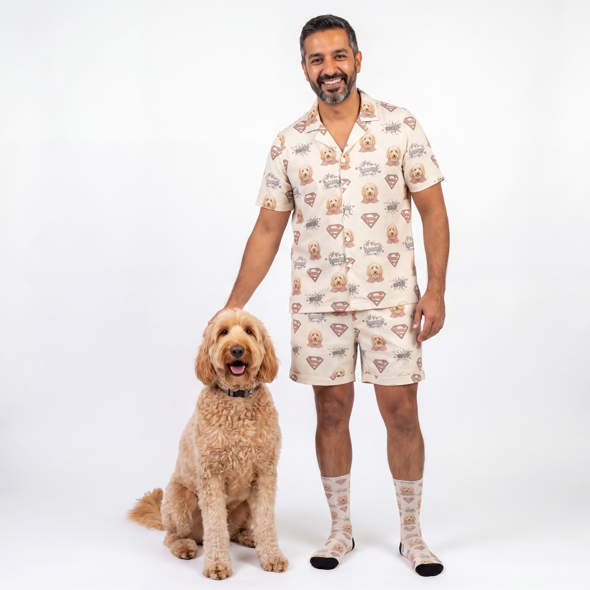 Man wearing superman pajama set with dog patterns standing next to a dog on a white background