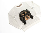 A light heather gray long-sleeve crewneck sweatshirt featuring a detailed graphic print of a black and tan Cavalier King Charles Spaniel dog on the front, displayed flat against a white background.