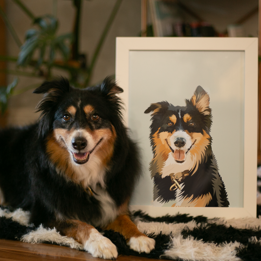 Black, tan, and white dog lying on a black-and-white rug next to a framed illustrated portrait of itself. The portrait shows the same dog with a happy expression on a light background, and the scene is set indoors with soft lighting and plants in the background.