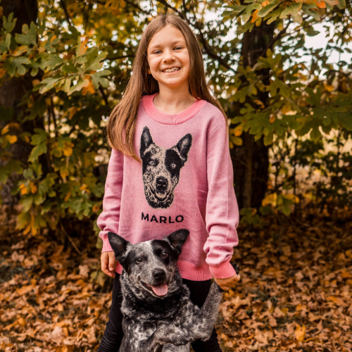 Girl wearing a pink sweater with a dog illustration and 'Marlo' text, standing with a dog