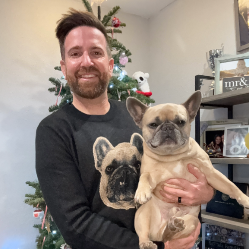 Man holding a dog wearing a black knit sweater