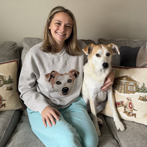 Woman sitting on a couch with a dog, wearing a sweater with a dog design.