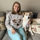 Woman sitting on a couch with a dog, wearing a sweater with a dog design.