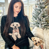 Woman wearing a sweater with a dog design, sitting next to a small dog.