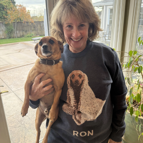 Woman holding a dog wearing a sweatshirt with a dog design, standing indoors.