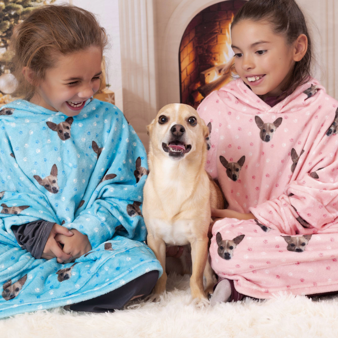 A woman sitting comfortably on a light-colored sofa, wearing a gray pajama dress printed with small dog faces and polka dots.