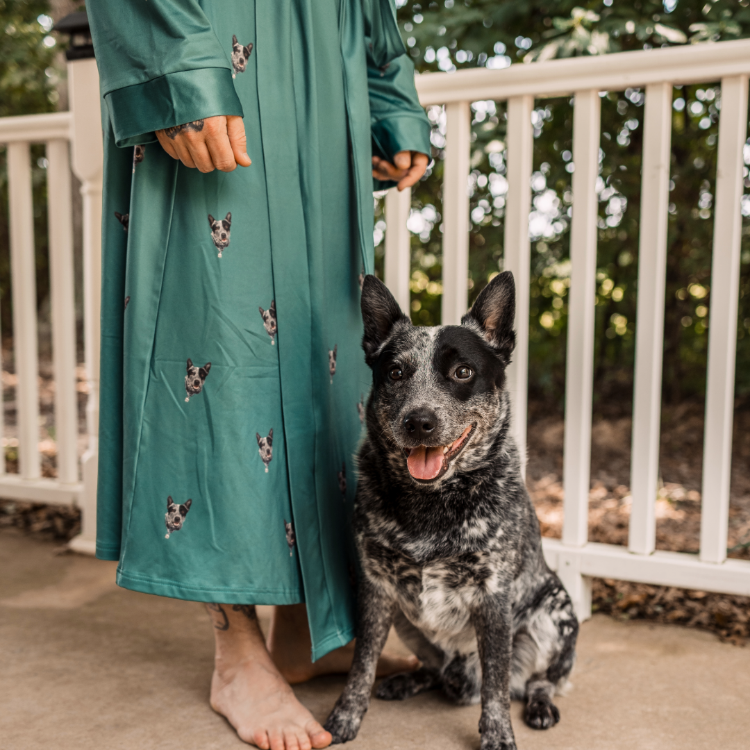 Person wearing a green robe with dog patterns standing next to a black and white dog on a porch.
