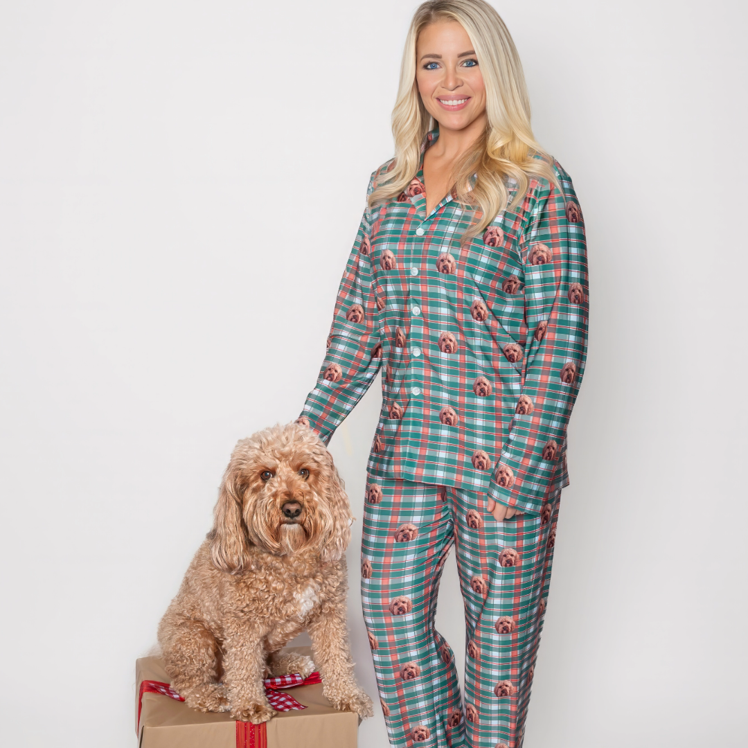 A woman wearing matching green and red plaid pajamas with a custom dog face pattern stands next to a fluffy apricot-colored dog sitting on a wrapped gift box. Both are posing against a plain white background.