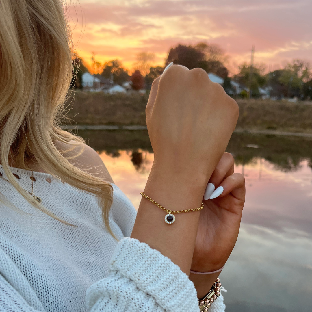 Person wearing a gold bracelet with a black stone against a sunset background