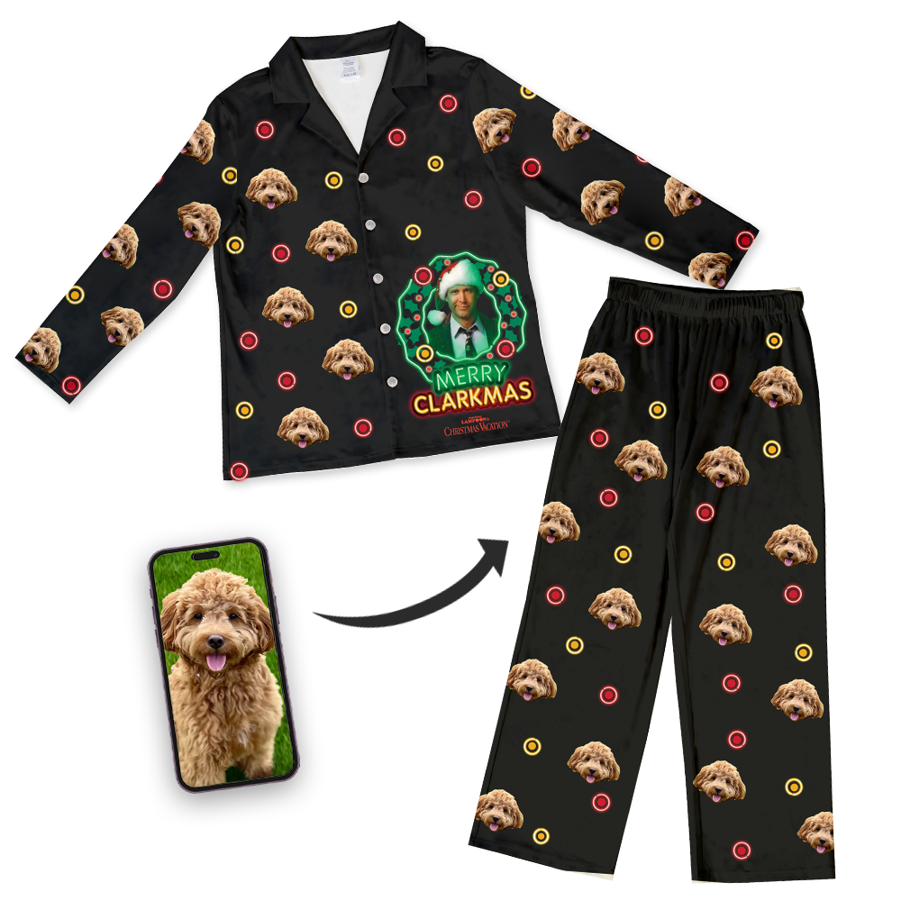 Black button-down pajama set featuring a repeating dog's face pattern with red and yellow Christmas baubles and a 'Merry Clarkmas' design showing a man in a Santa hat from 'National Lampoon's Christmas Vacation', displayed alongside a smartphone with the dog's photo and an arrow indicating customization.