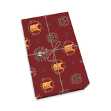 A rectangular gift box wrapped in dark red holiday paper with a repeating pattern of gold jester figures and small green accents, tied with a simple brown string bow on a white background.