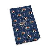 A gift-wrapped rectangular package tied with twine on a plain white background. The wrapping paper is dark navy blue with a repeating pattern of Santa Claus faces in Santa hats, white snowflakes, and small green and pink holiday motifs.