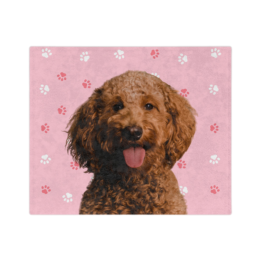 A blanket with a pink background and paw prints, featuring a centered, smiling portrait of a dog.