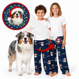 Two children wearing matching navy blue Christmas dog pajama pants with a dog print, standing barefoot on a white background next to an Australian Shepherd dog. A circular inset shows a dog wearing a Santa hat with holiday lights, and a red arrow points from the inset to the pants pattern.