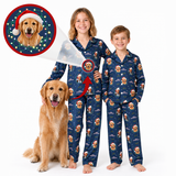 Two children wearing matching navy blue Christmas-themed pajamas with a golden retriever dog print, standing barefoot on a white background. A golden retriever sits beside them, and a circular inset shows a close-up of the dog print with a Santa hat.