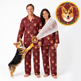 A man and a woman wearing matching burgundy pajamas with a corgi face print, standing barefoot on a white studio background. A corgi dog is jumping up on the left, and a circular inset at the top right shows a close-up of the corgi face design on the pajama.