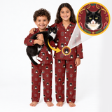 Two children wearing matching burgundy pajamas with a black-and-white cat print, standing barefoot on a white studio background. One child holds a black-and-white cat, and a circular inset shows a custom cat portrait design that appears on the pajama chest.