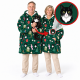 Two adults wearing matching green holiday-themed cat-print hooded robes, standing against a white studio background. One adult holds a black-and-white cat, and the image includes an inset circle showing a close-up of the cat motif on the robe.