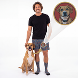 A man stands next to a dog on a white studio background, wearing patterned shorts and socks, with a magnified inset showing the dog portrait printed on the shorts.