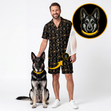 A man wearing a black short-sleeve button-up shirt and matching shorts with a repeating dog-face pattern, standing next to a German Shepherd wearing a yellow collar. A circular inset at the top right shows a close-up of the dog-face print on a black background.