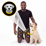 A man kneels beside a golden retriever dog on a white studio background, wearing patterned shorts with a dog collar graphic and pointing to the dog's collar with a yellow arrow. A circular inset shows a dog wearing a yellow collar.