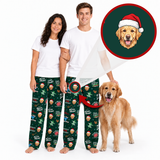 A man and a woman wearing matching white t-shirts and dark green Christmas pajama pants with a cartoon dog print, standing barefoot against a white background next to a golden retriever dog. A circular inset shows a custom dog portrait wearing a Santa hat.