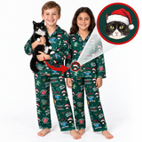 Two children wearing matching green Christmas-themed pajamas with a cat print, standing against a white background. One child holds a black and white cat, and an inset circle shows a close-up of a cat wearing a Santa hat with the text 'Meow'.